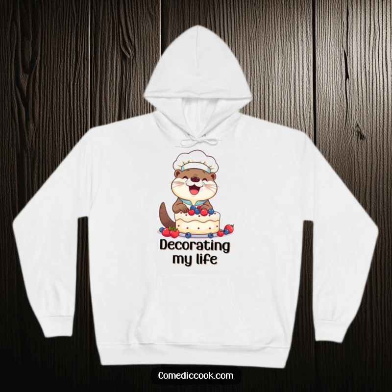 Funny Otter Chef Hoodie: Smiling otter happily decorating a cake with berries, offering warmth and sweet humor.