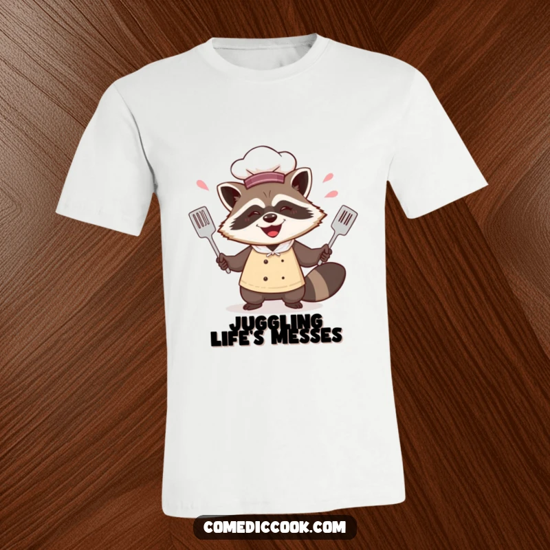 Funny happy raccoon chef t-shirt depicting him juggling spatulas with a gleeful, mischievous grin, celebrating kitchen antics.